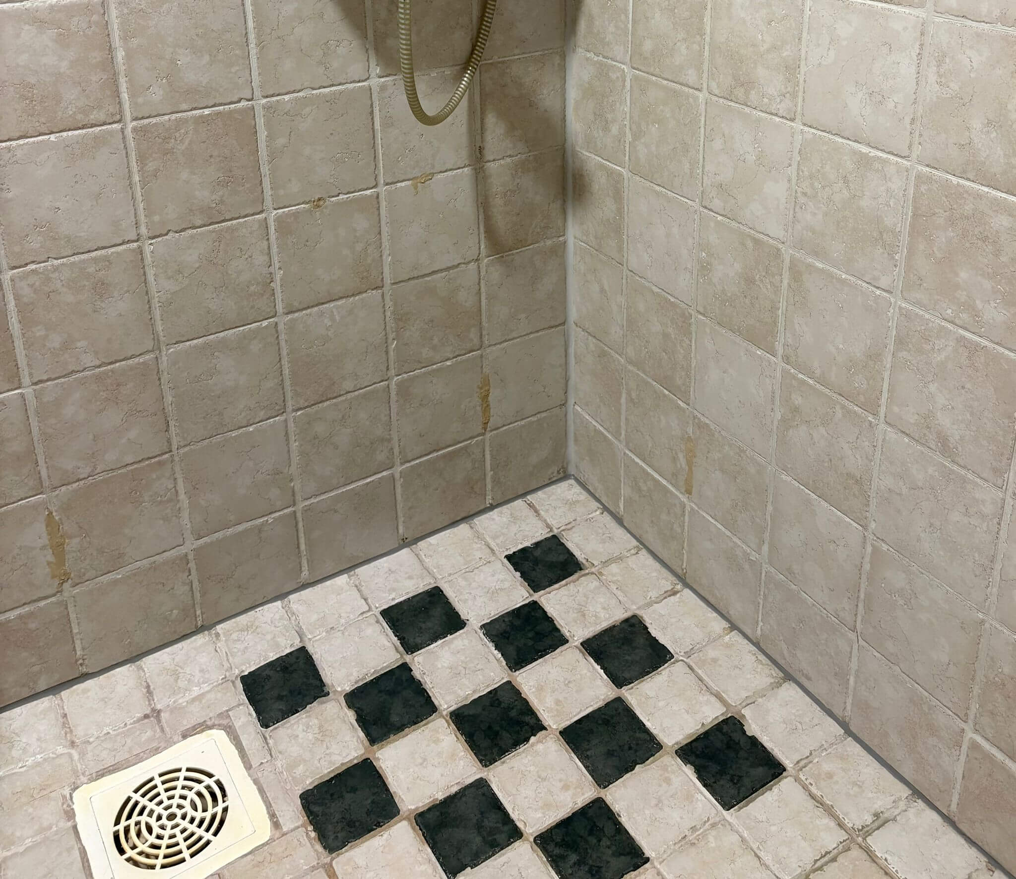 Kylpyhuoneen suihkun lattia, jossa vaaleat ja tummanharmaat ruutukuvioidut laatat sekä valkoinen lattiakaivo.